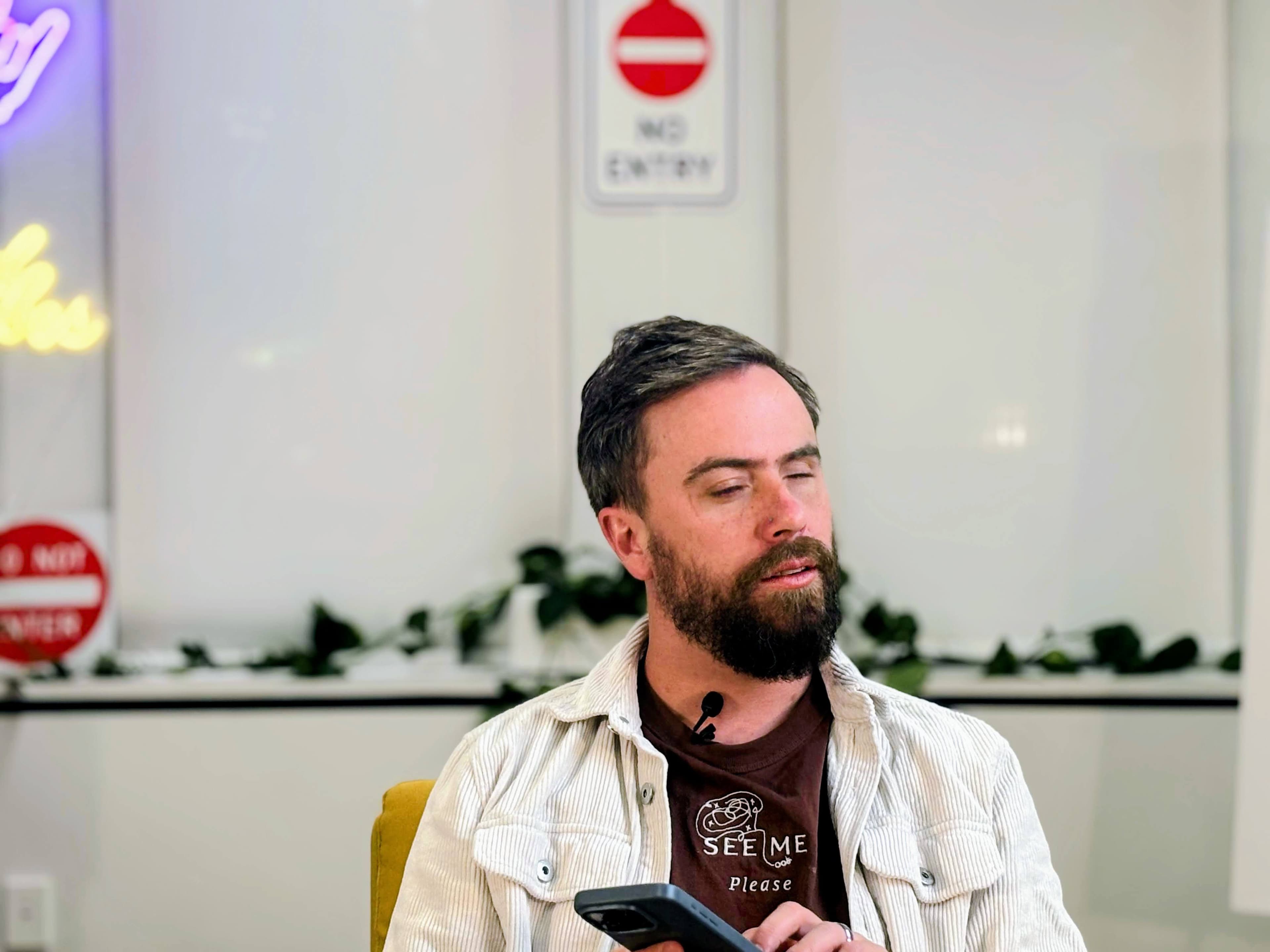 One of our valued blind user testers in a white corduroy jacket over a brown See Me Please t-shirt smiling