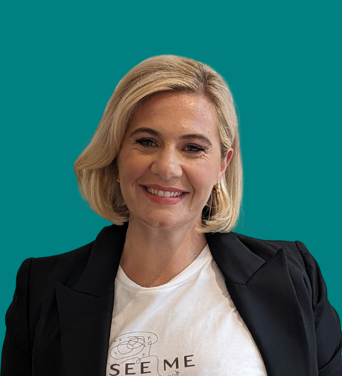 Smiling, with short blonde hair, wearing a See Me Please t-shirt.